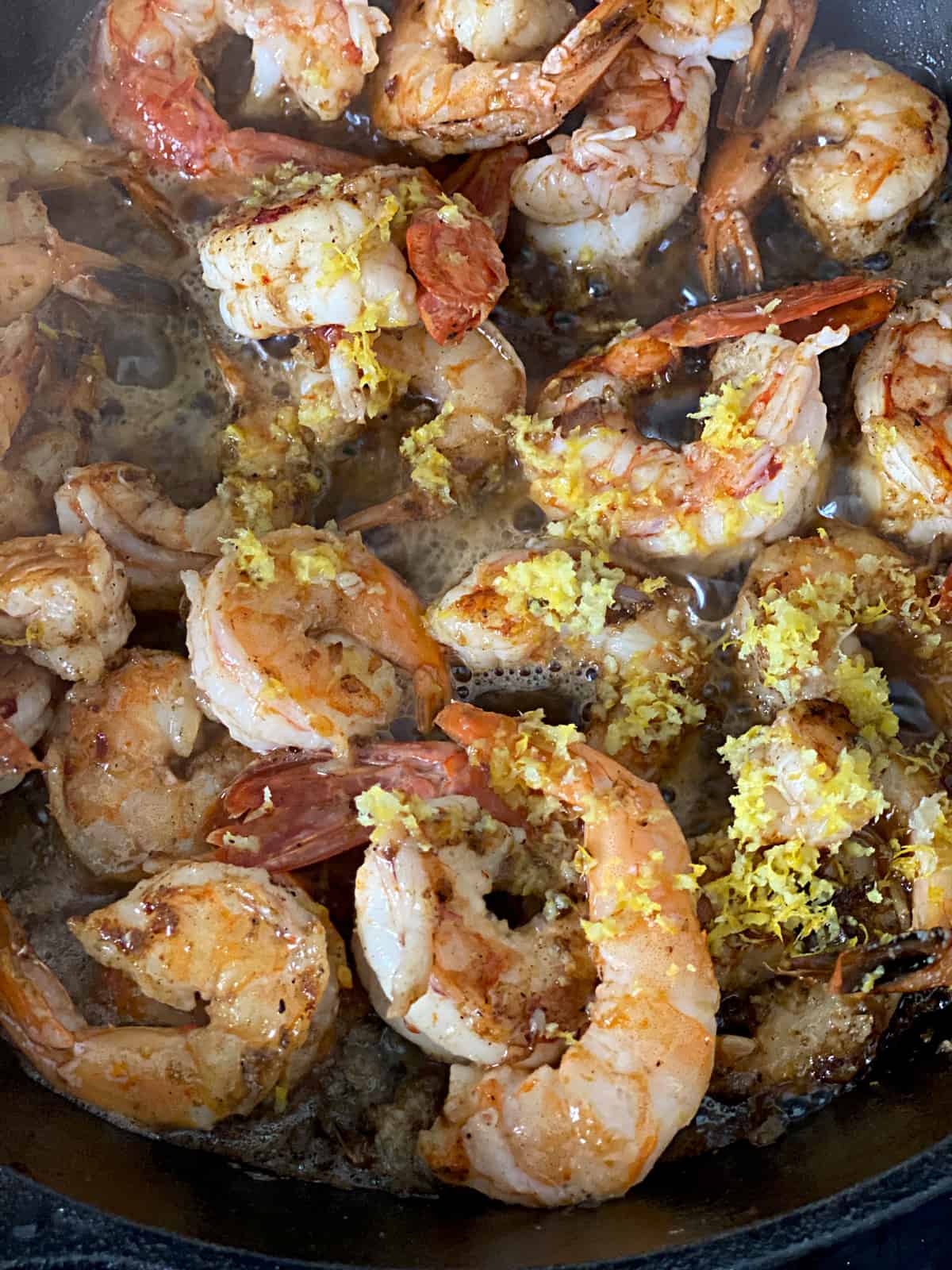 Shrimp in a skillet sautéing with lemon zest and butter.