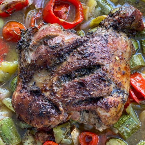 A boneless leg of lamb in a baking pan surrounded with vegetables in a broth.