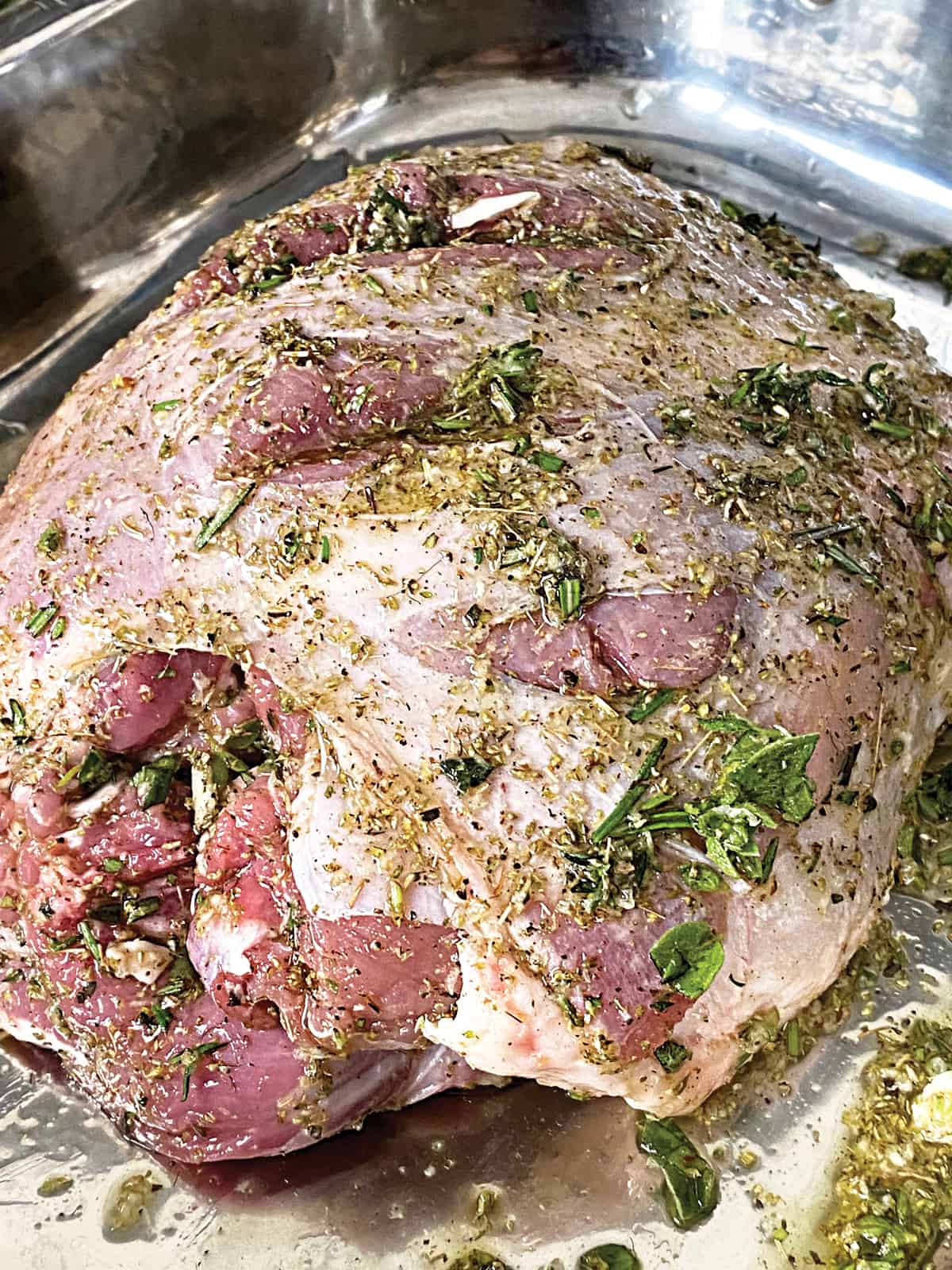 A boneless lamb shoulder marinating with olive oil and herbs.