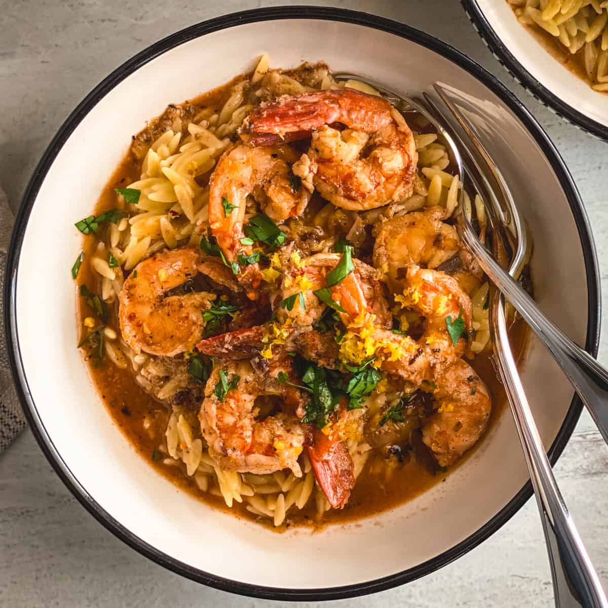 Shrimp orzo in lemon garlic butter sauce in a white bowl with parsley, lemon zest