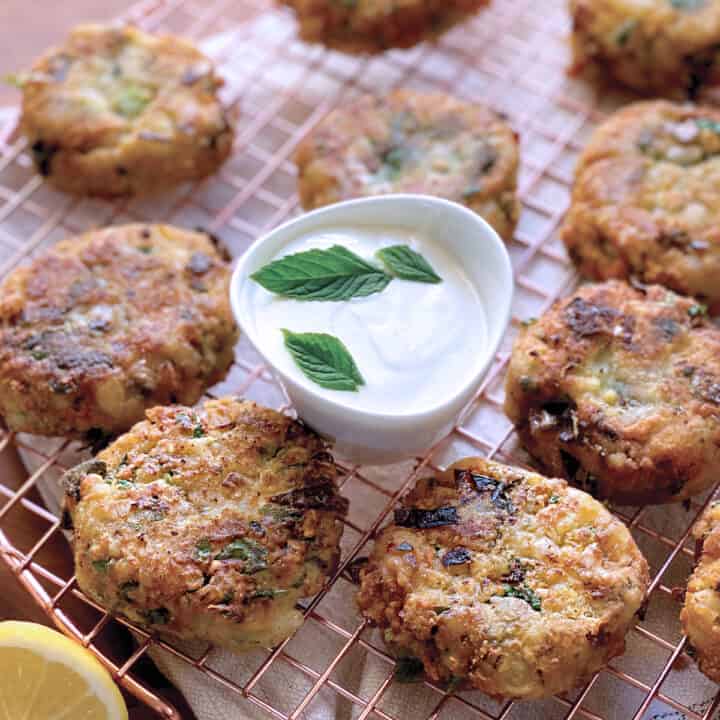 Chickpea fritters on a wire rack over a cloth, a lemon wedge and a bowl with yogurt sauce.