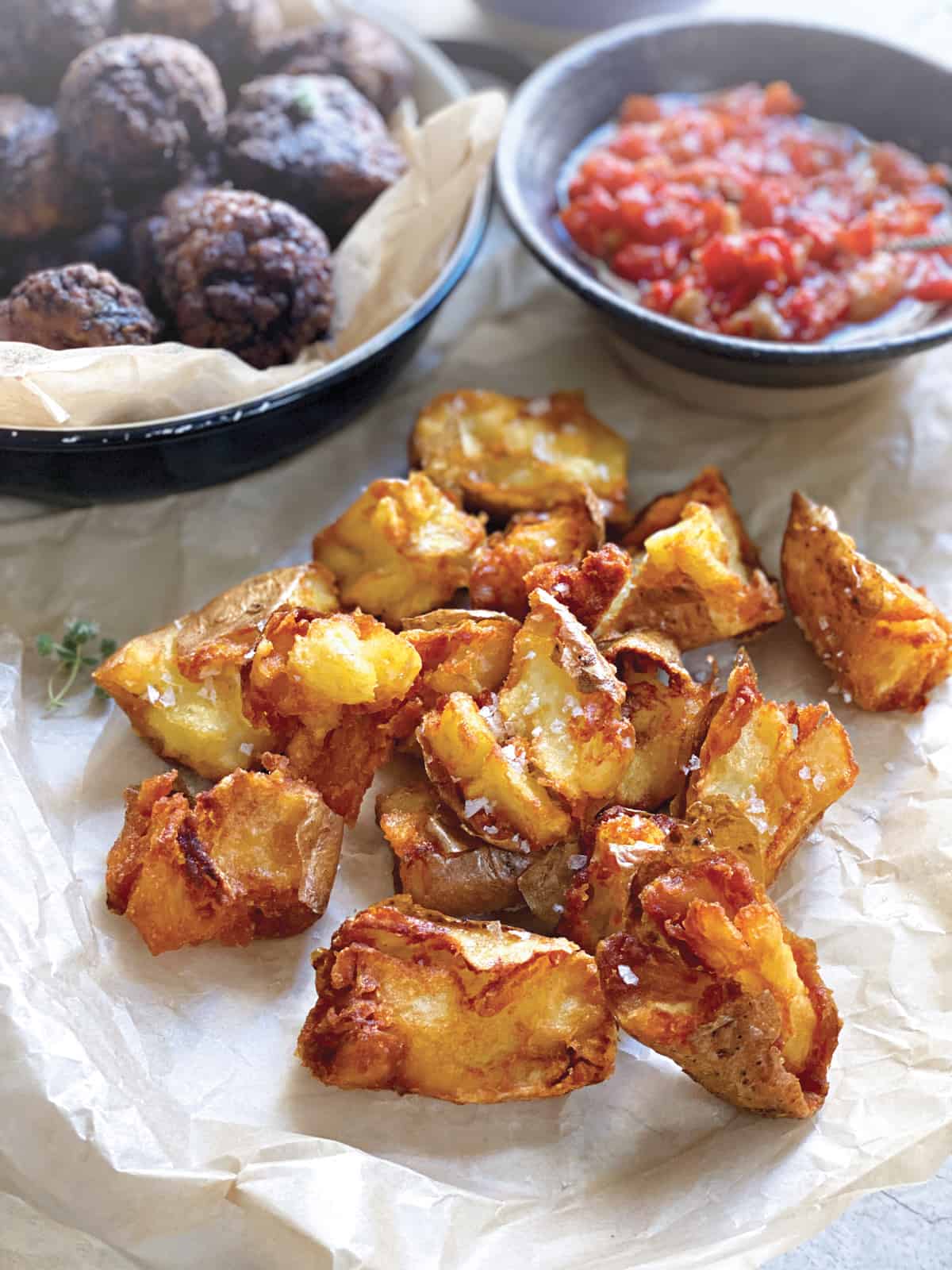 Country fried potatoes on a parchment paper, a bowl with keftedew and salsa at the back.