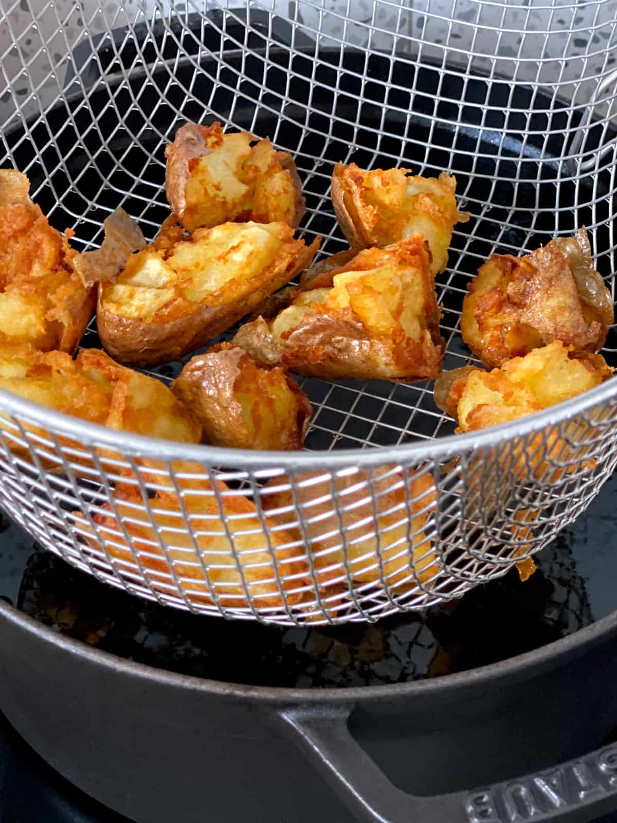 A wire basket over a hot dutch oven draining fried potatoes.