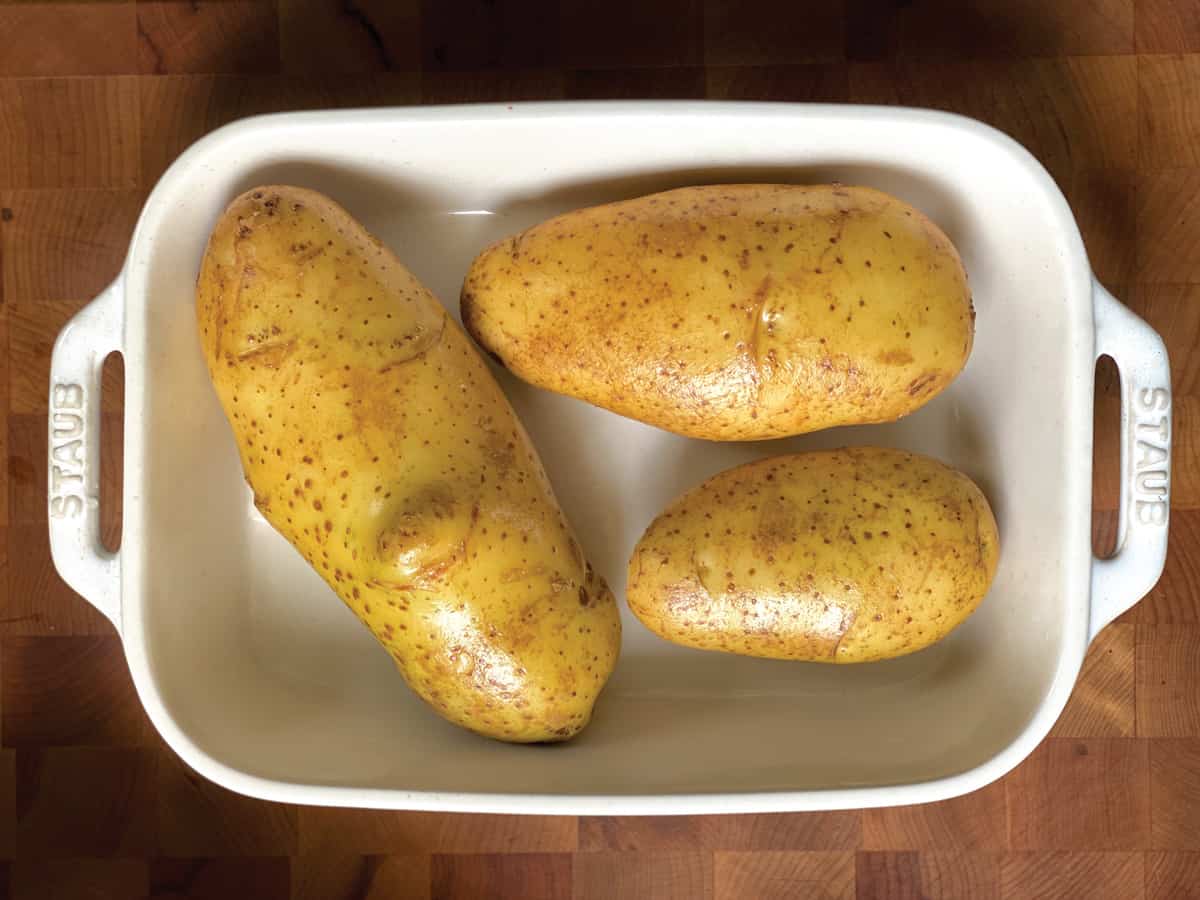 Six potatoes in a white baking pan.