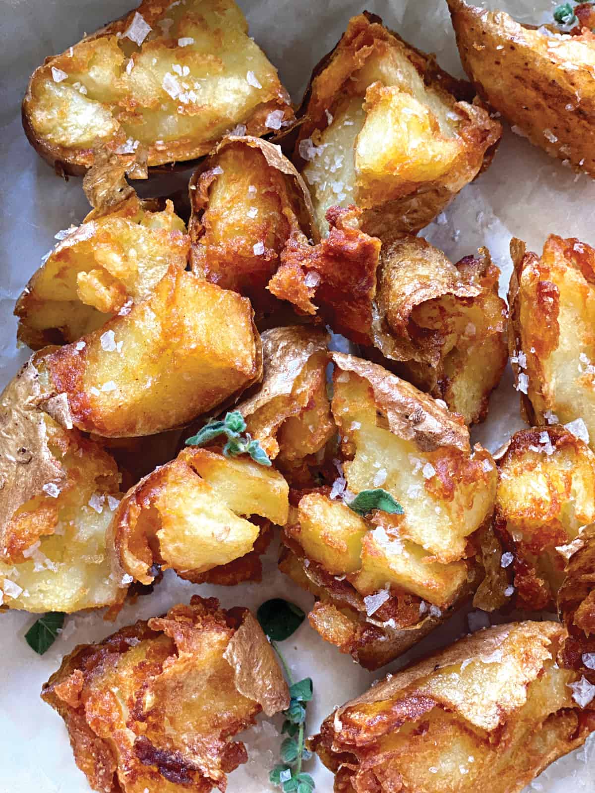 Crispy country potatoes on parchment paper with fresh oregano and sea salt.