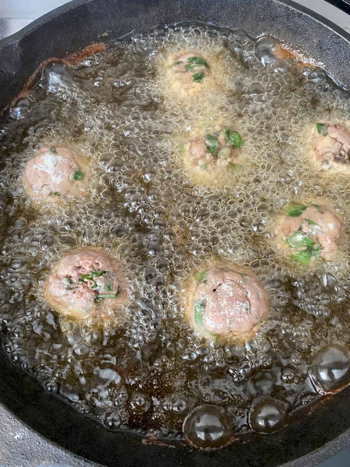 Meatballs frying in a cast iron pan.