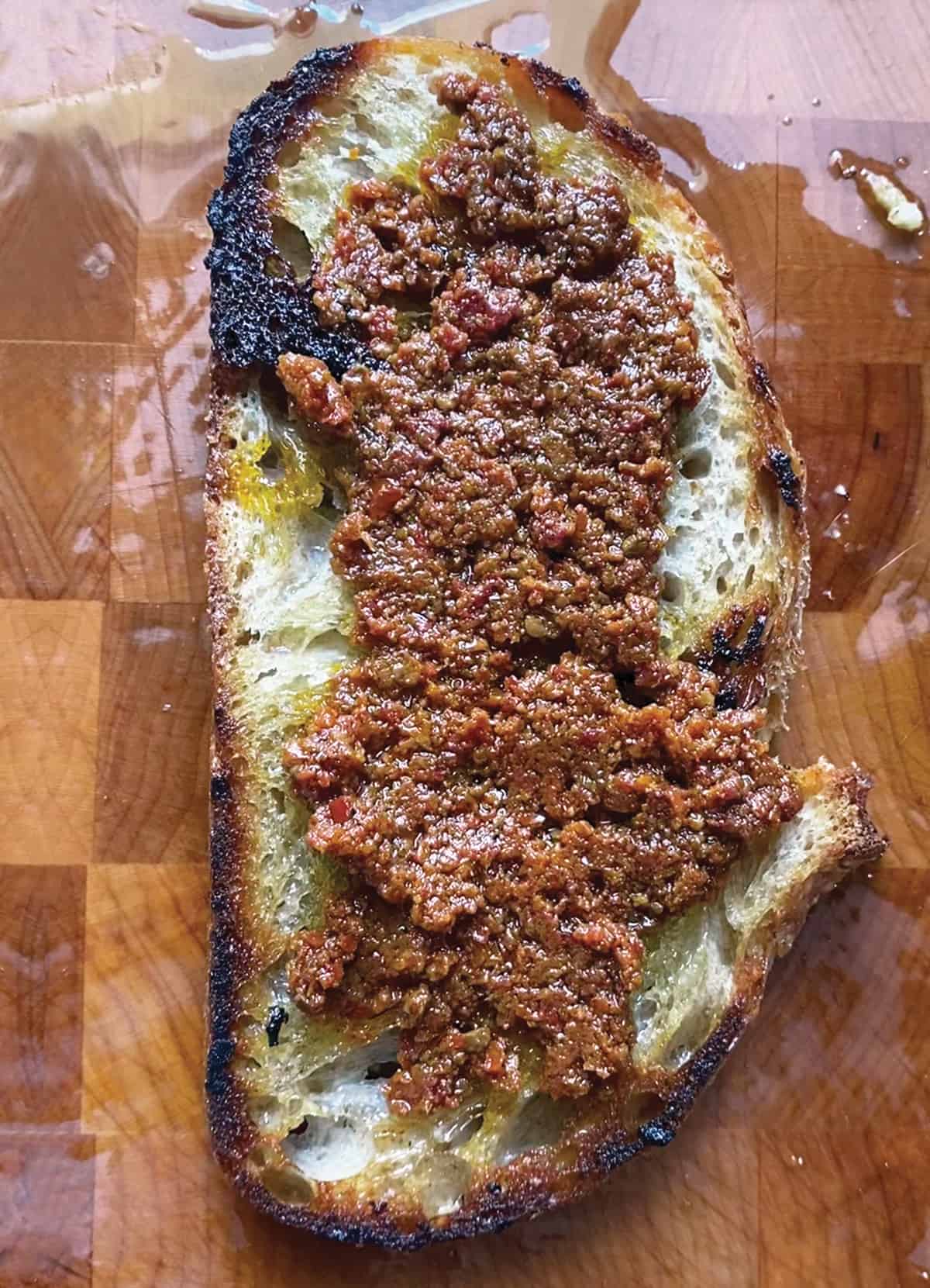 A piece of toasted bread with red pesto on a wooden surface.