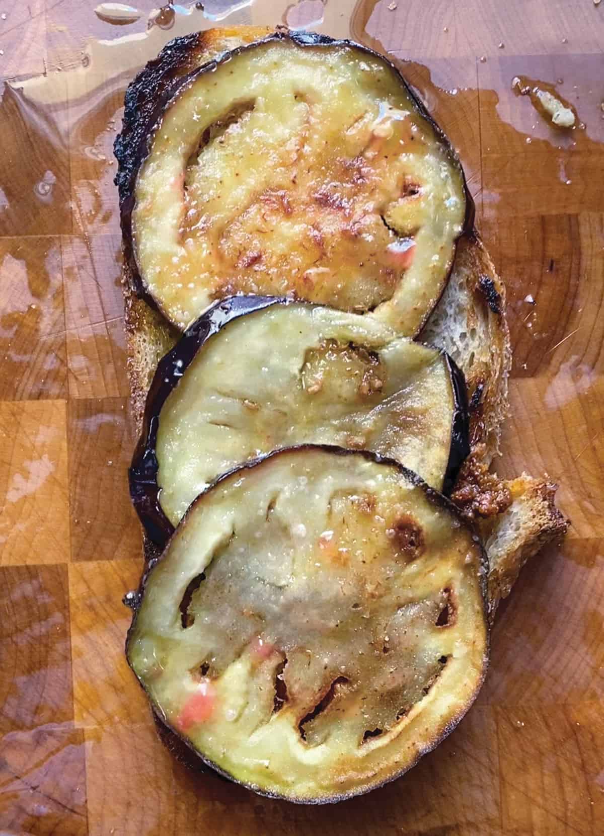 An open sandwich with eggplant slices on a wooden surface.