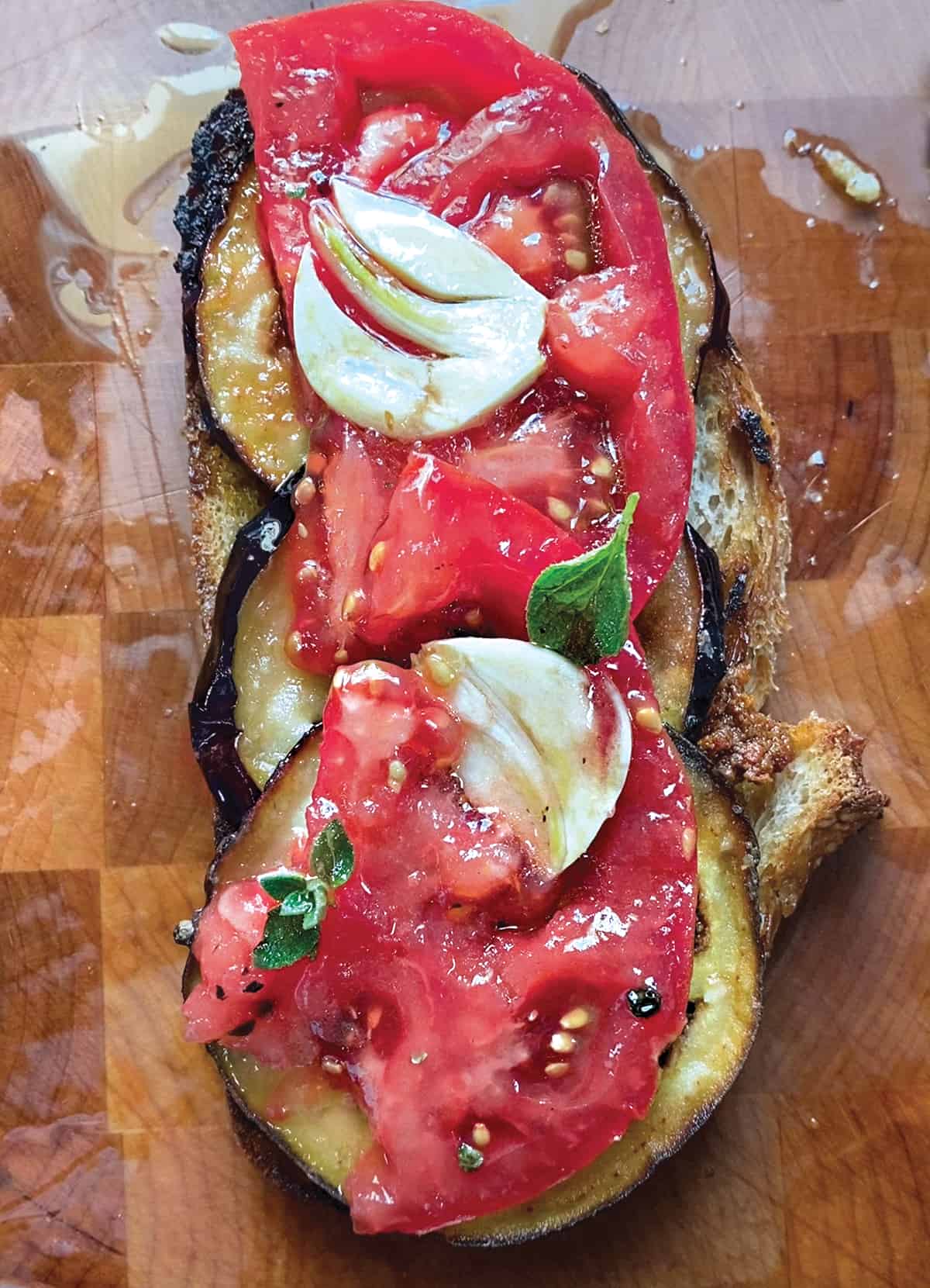 An open sandwich with eggplant, and tomatoes on a wooden surface.