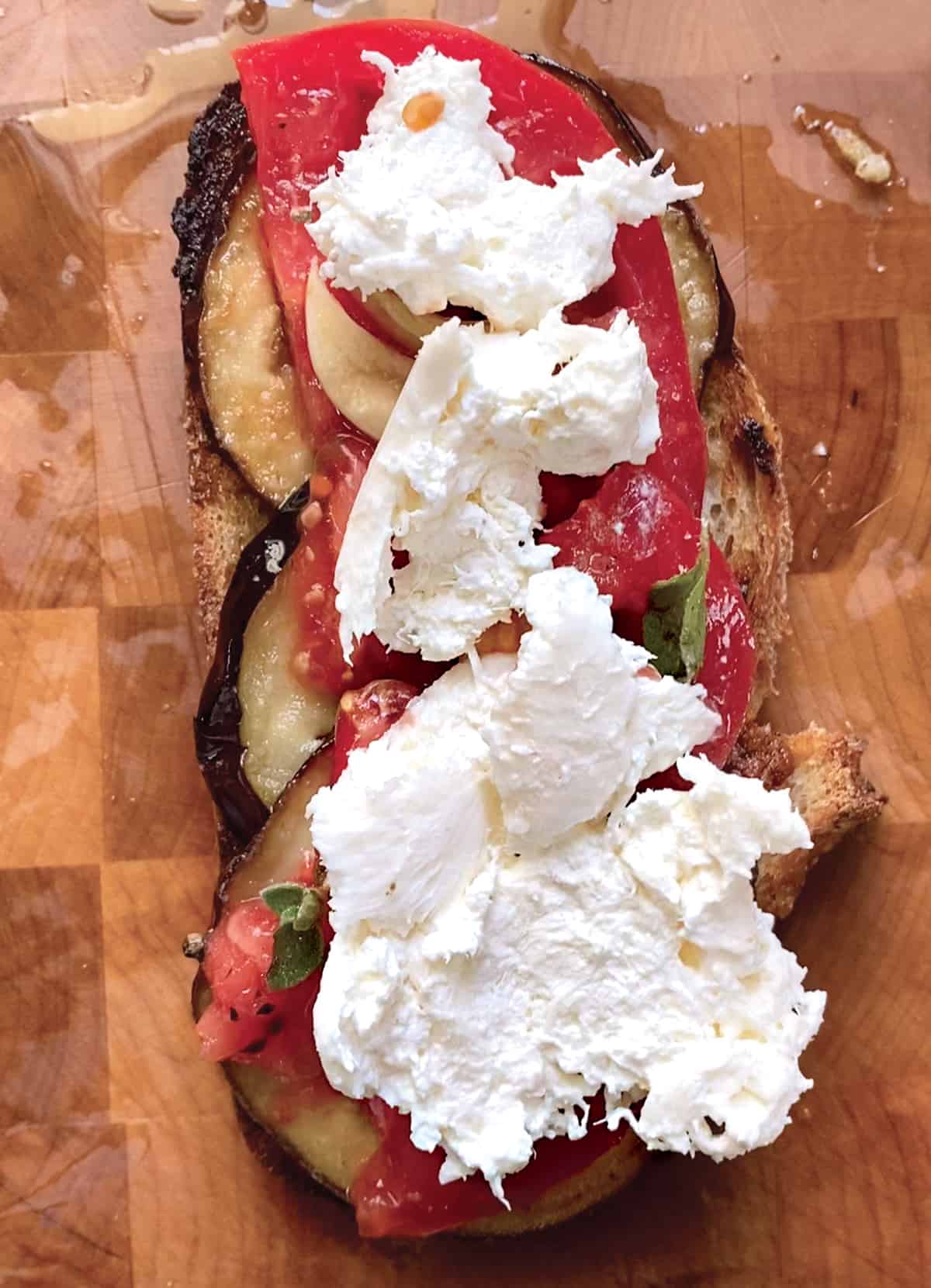 An open sandwich with with eggplant, tomatoes and mozzarella on a wooden surface.