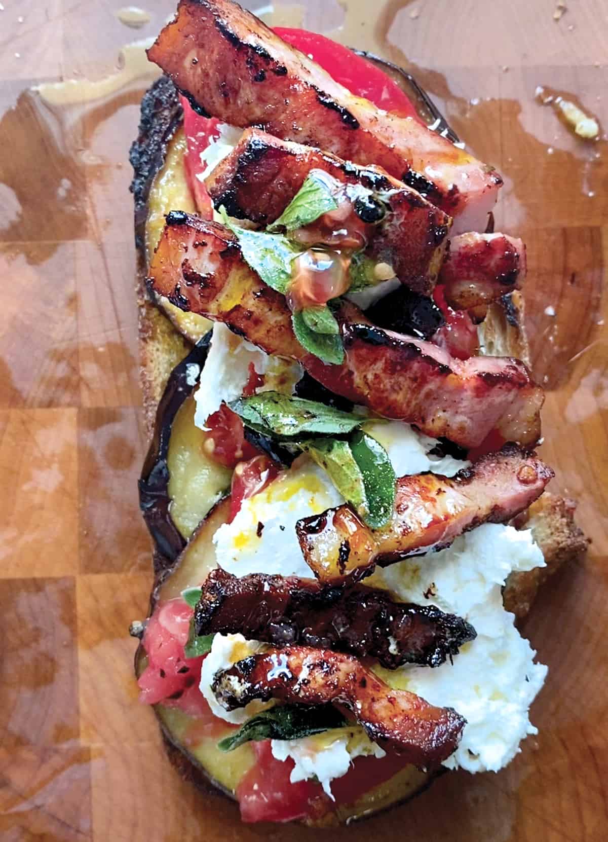 An open-faced tomato eggplant sandwich with pancetta on a wooden surface.