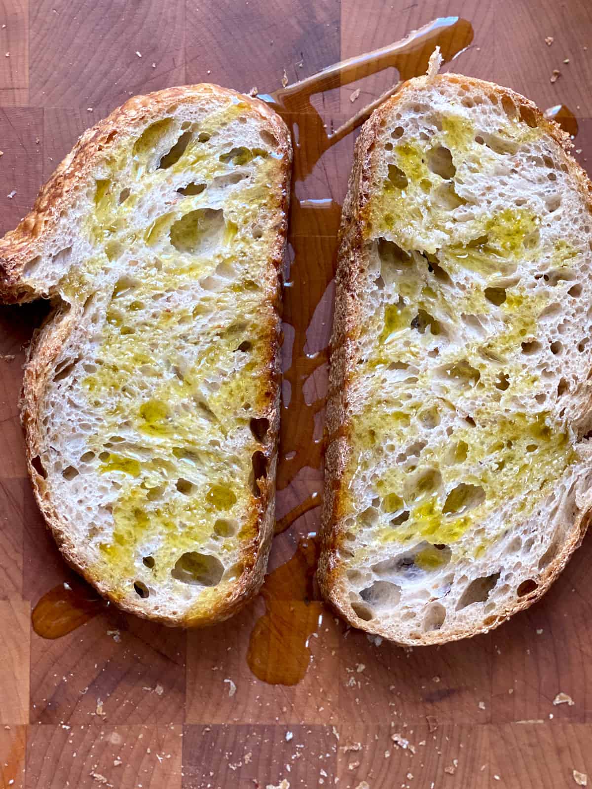 Two slices of bread with olive oil on a butcher block.