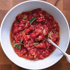 A bowl with red pepper and tomato relish and a spoon.