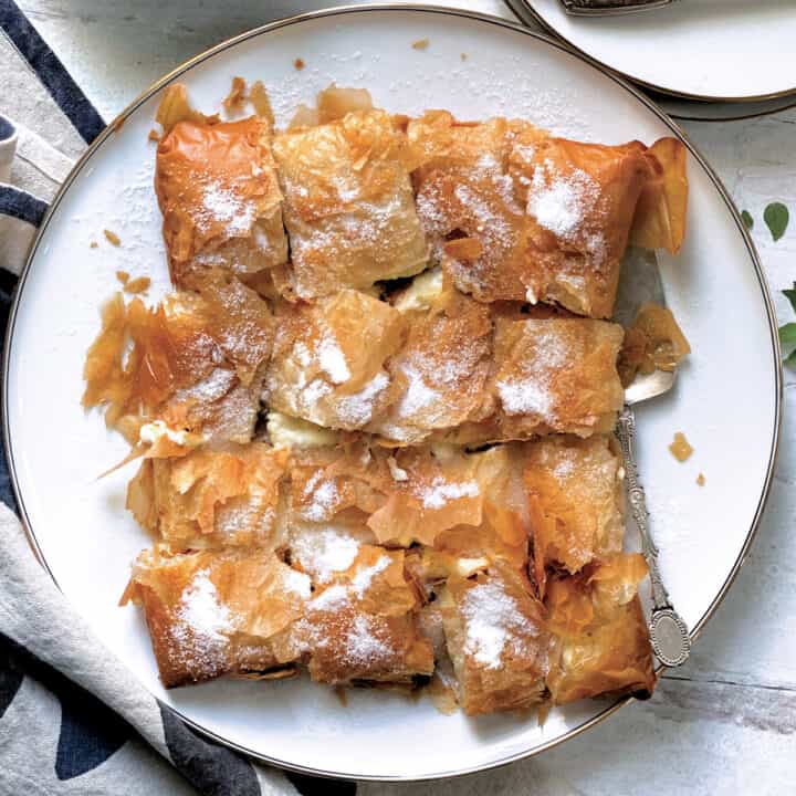 A plate with cut yp cretan bougatsa and a serving utensil on a white table.