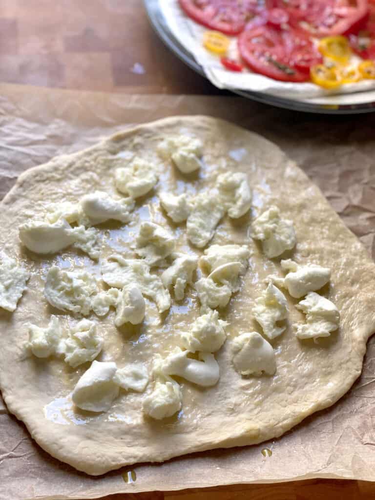 Pizza dough on parchment paper with shredded mozzarella on top.