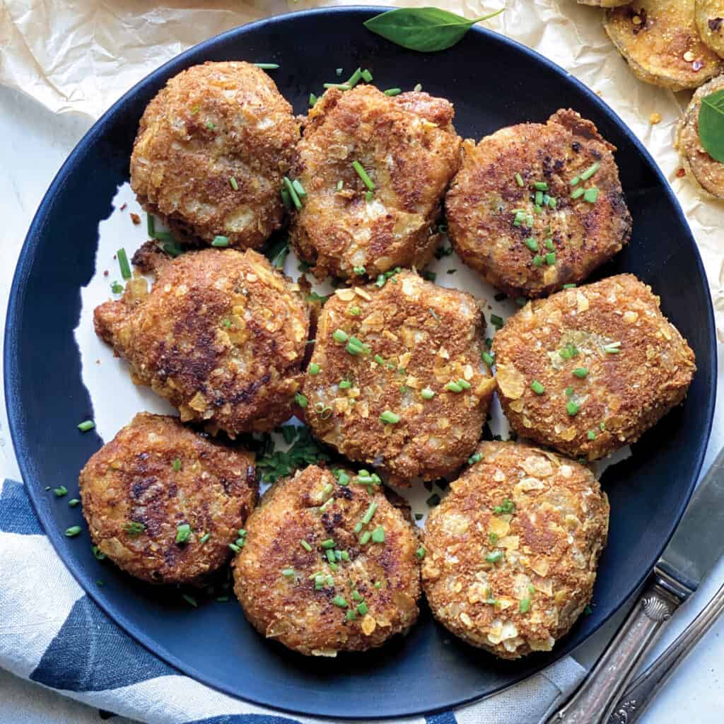 A plate with potato fritters, a cloth napkin and a knife and fork.