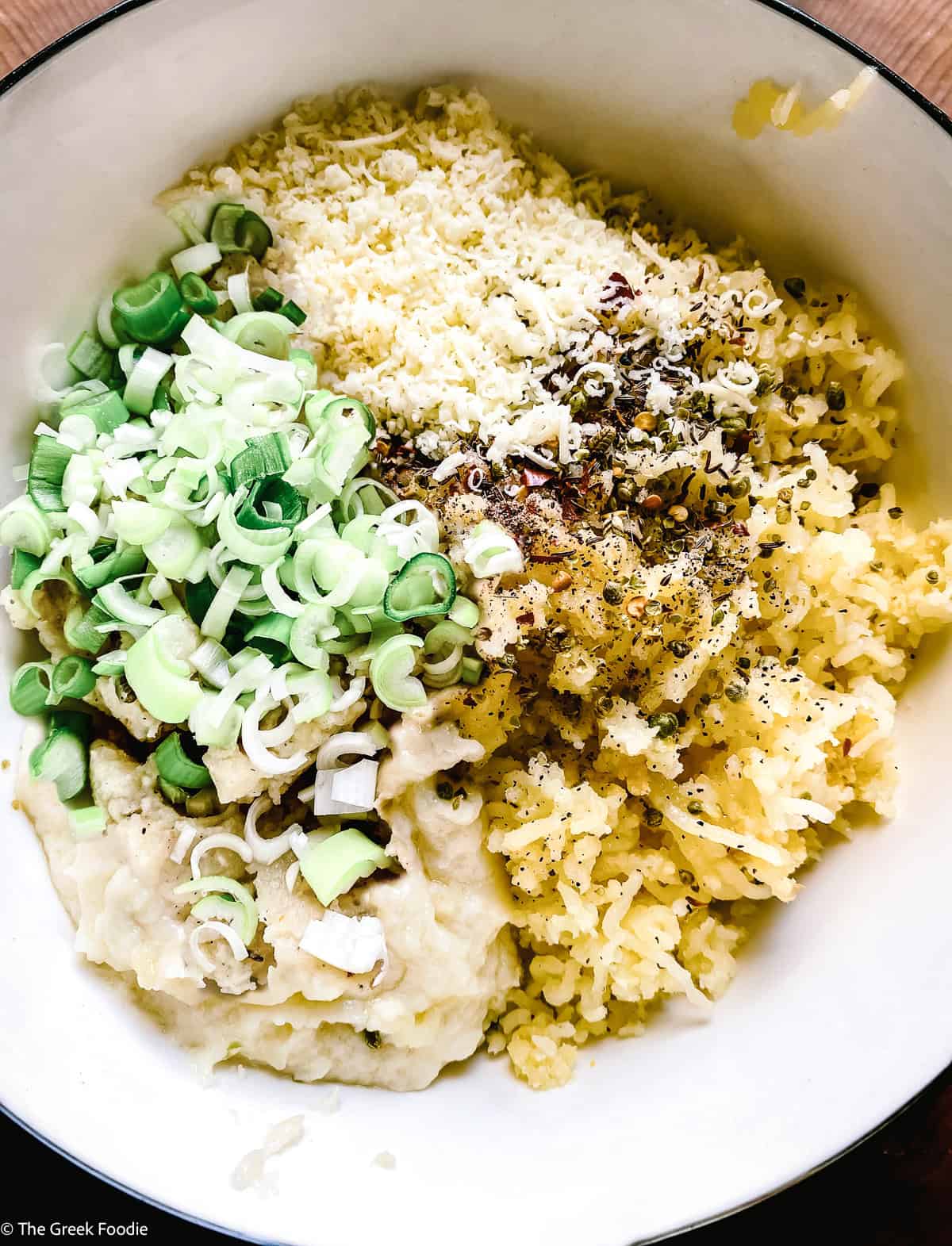 Mashed potato mixture in a bowl with scallions, grated kefalotyri cheese, béchamel, and herbs before mixing.