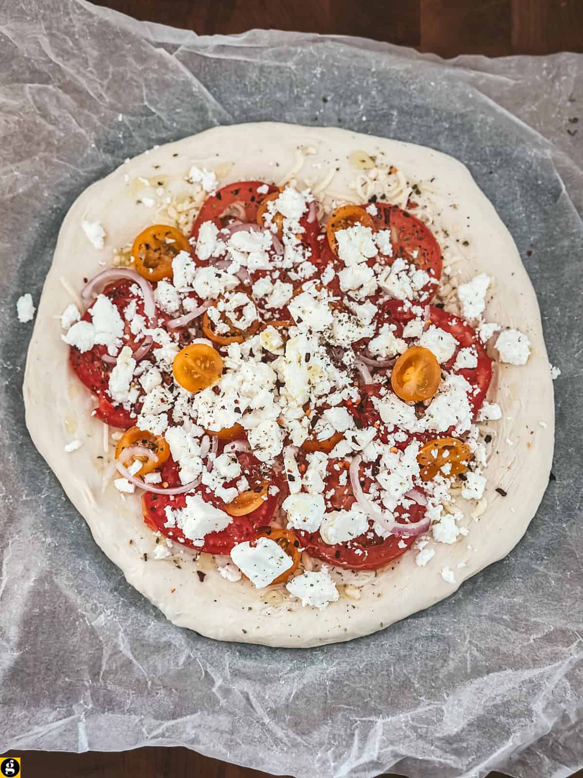 An assembled feta pizza, with lots of cheese and sliced tomatoes.