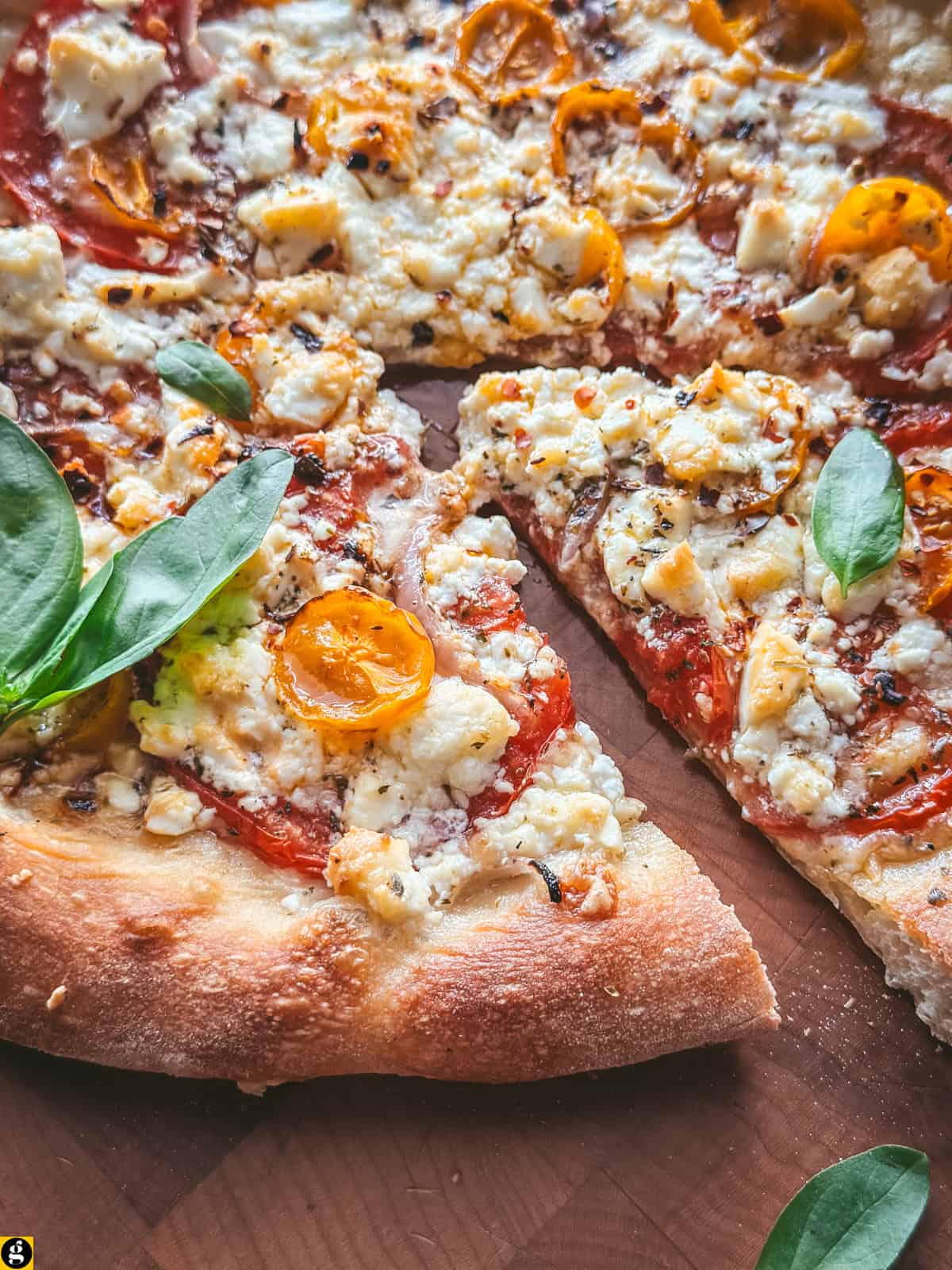 Slices of feta cheese pizza with yellow cherry tomatoes, chili flakes and fresh basil