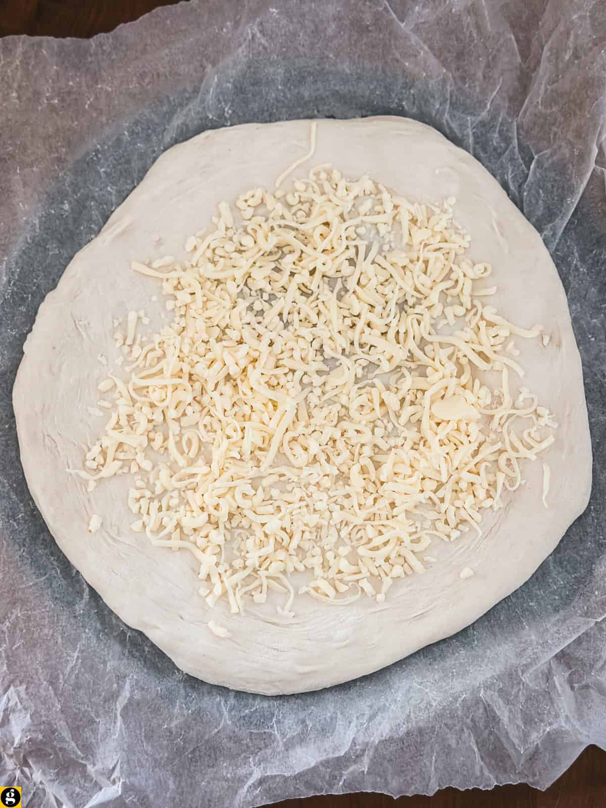 Pizza dough on parchment paper with shredded mozzarella on top.