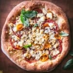 Overhead feta pizza with golden crumbled feta, red tomatoes, yellow cherry tomatoes and fresh basil on a wooden board