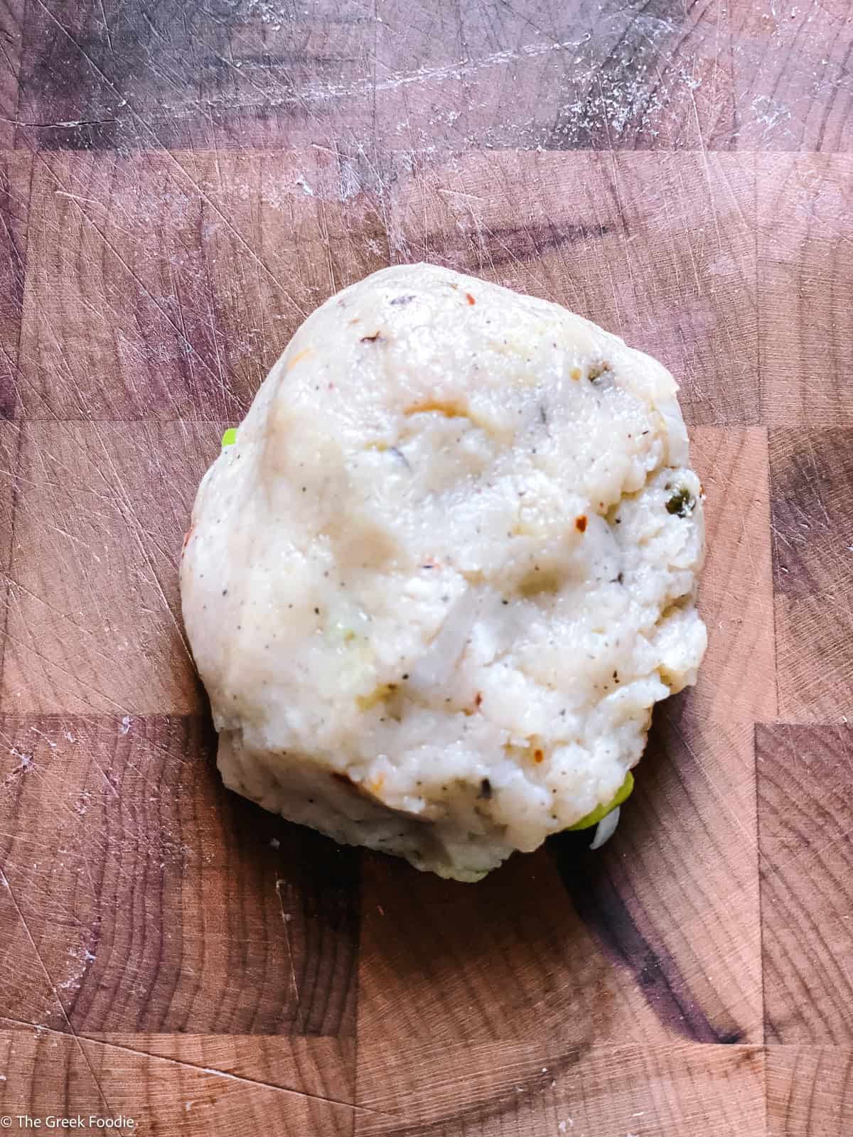 A shaped potato fritter ball on a wooden cutting board before coating.