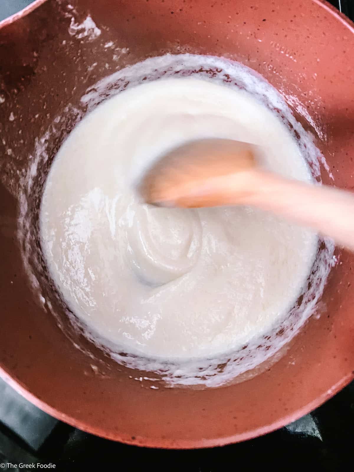 Béchamel sauce being stirred with a wooden spoon in a copper saucepan until smooth and thick.