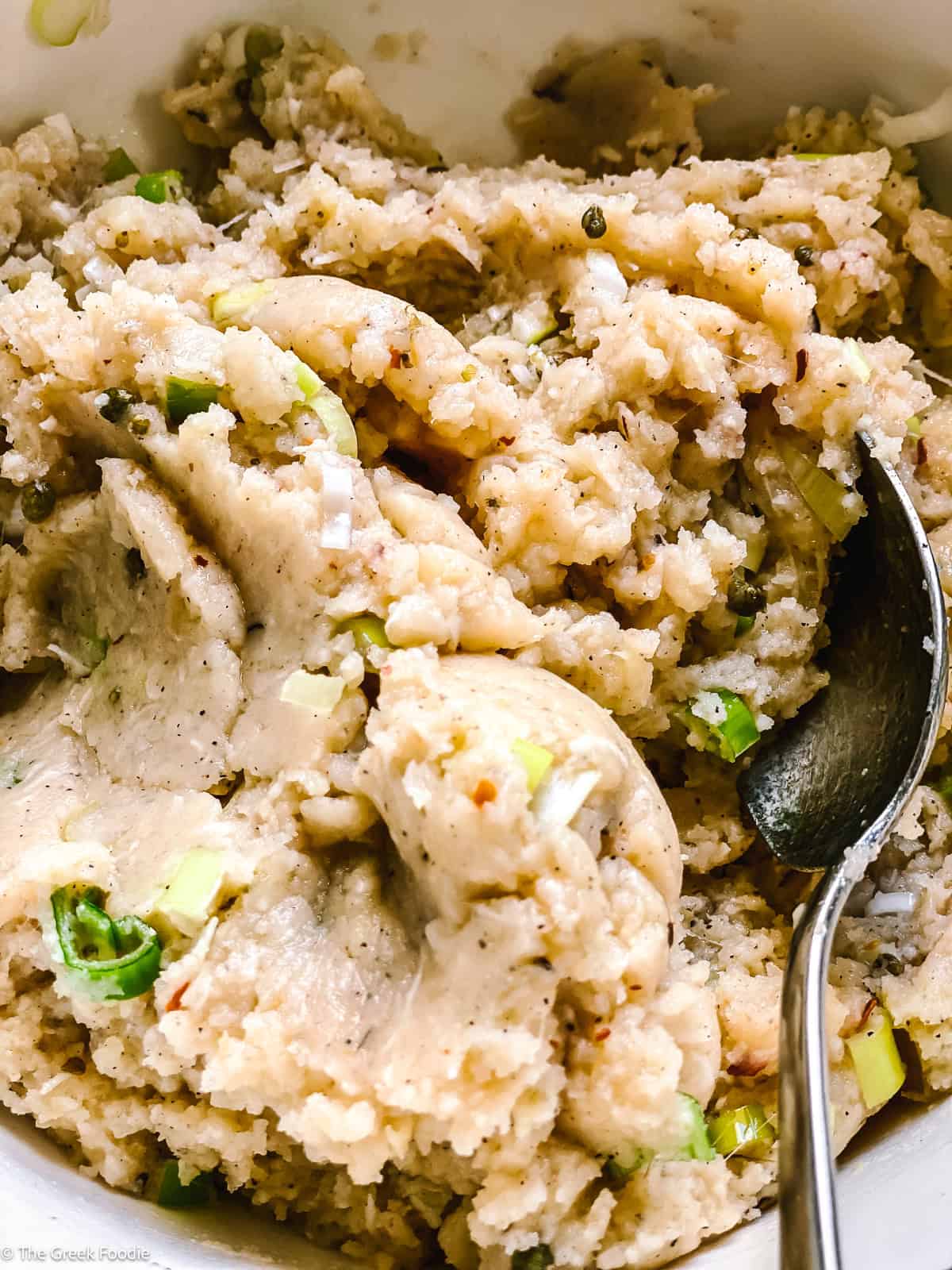 Close-up of the creamy potato fritter mixture showing herbs, scallions, and chili flakes throughout.