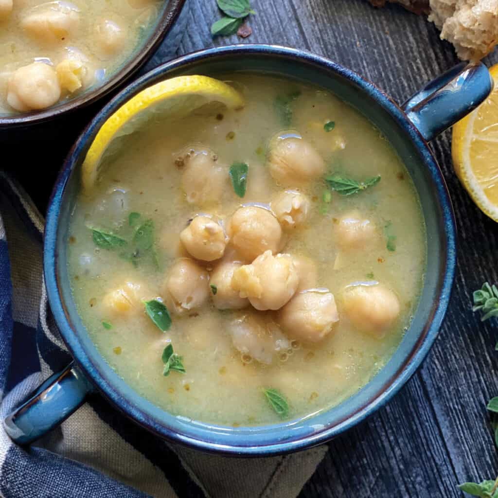Two blue bowls with chickpea soup, pieces of bread and lemons.