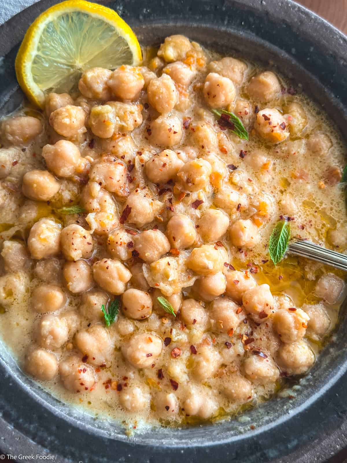 A bowl with chickpea soup, and a lemon slice.