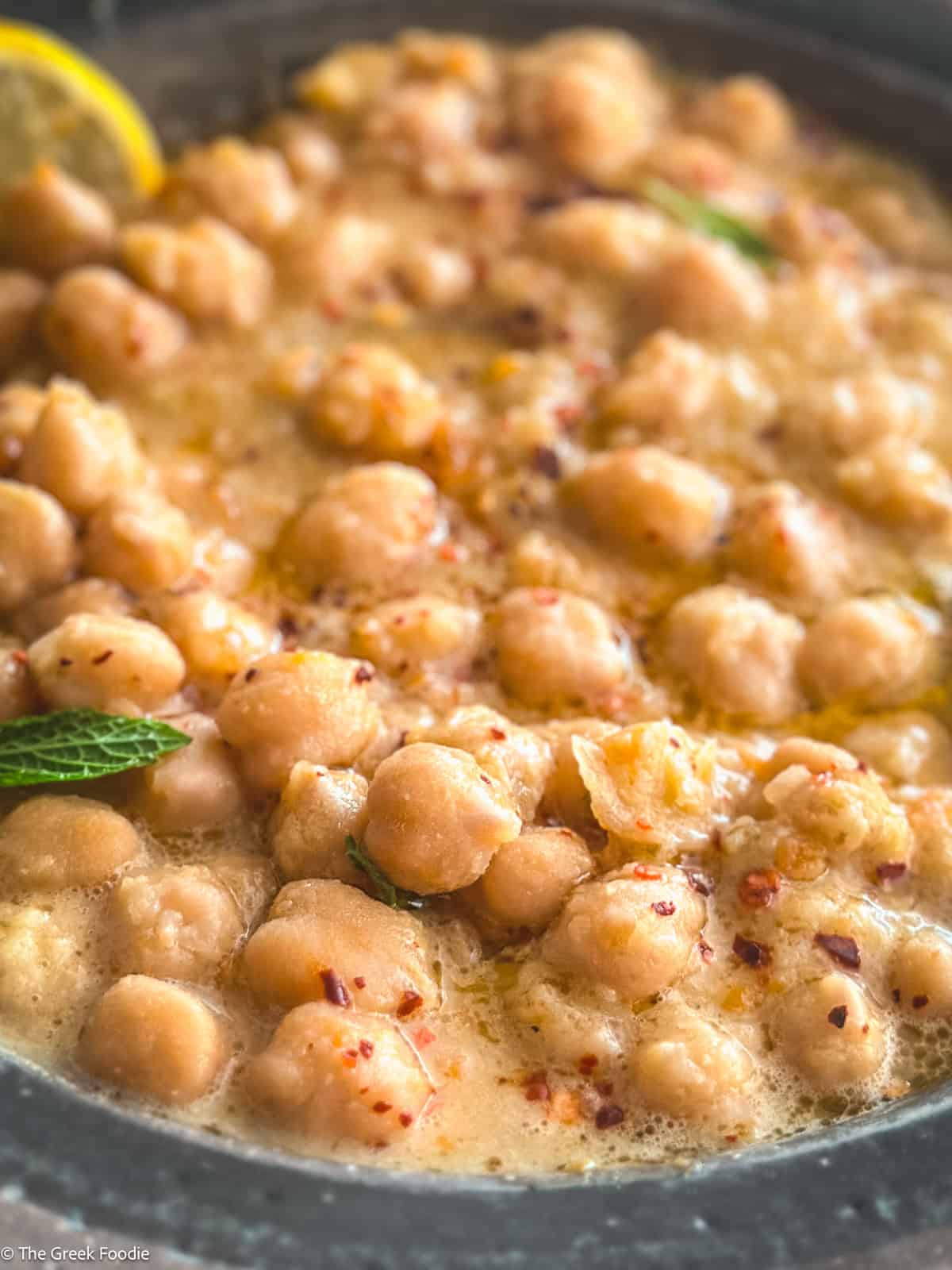 A bowl with chickpea soup, and a lemon slice.
