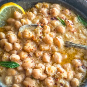 A bowl with chickpea soup, and a lemon slice.