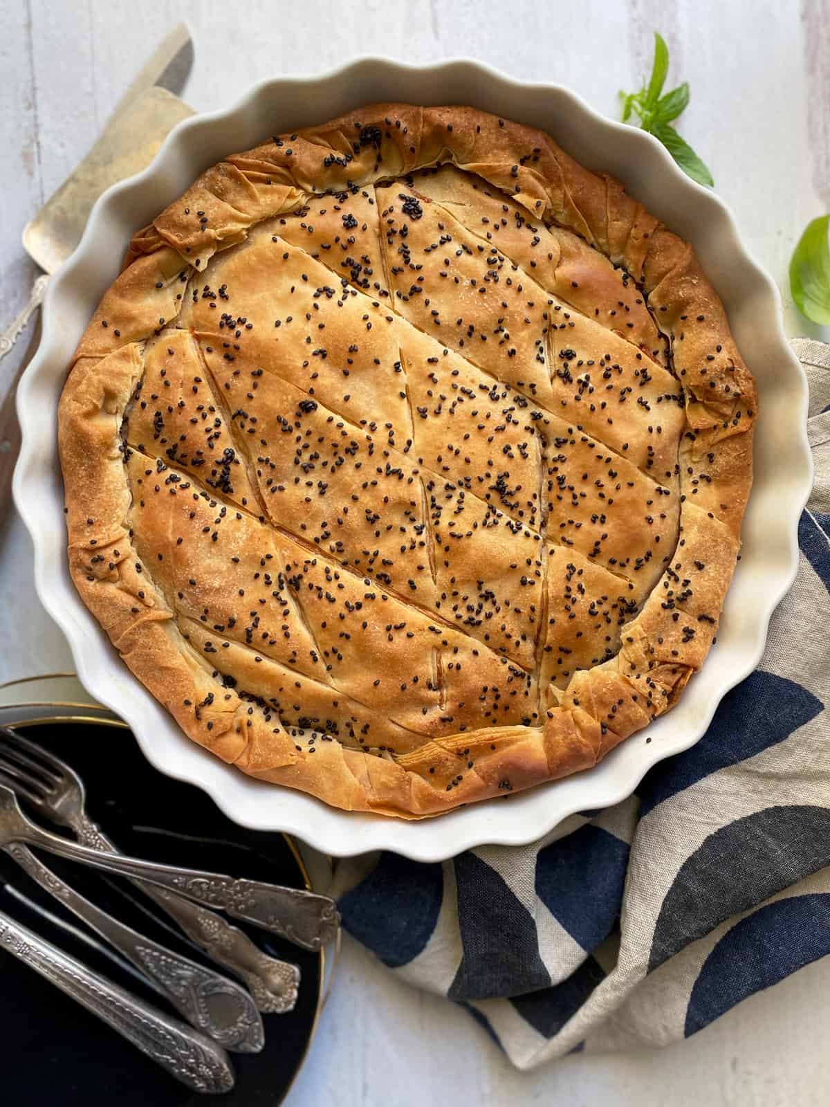 A greek pie with phyllo and sesame seeds, a napkin and utensils.