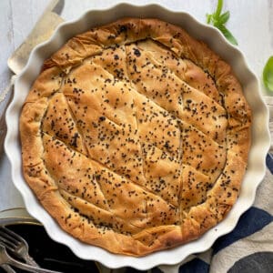 A greek pie with phyllo and sesame seeds, a napkin and utensils.