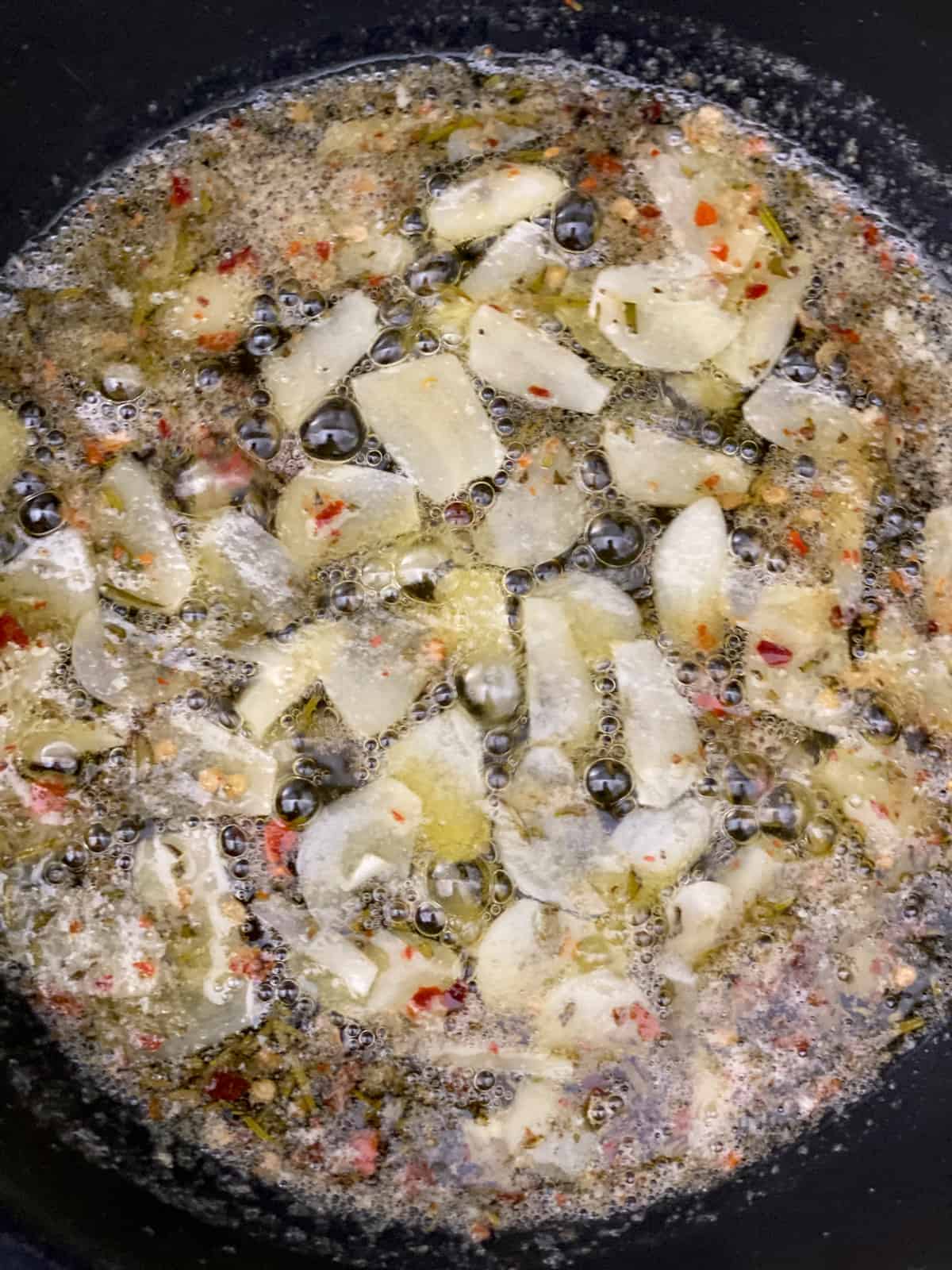 Sliced garlic, minced rosemary and seasonings with oil in a skillet.
