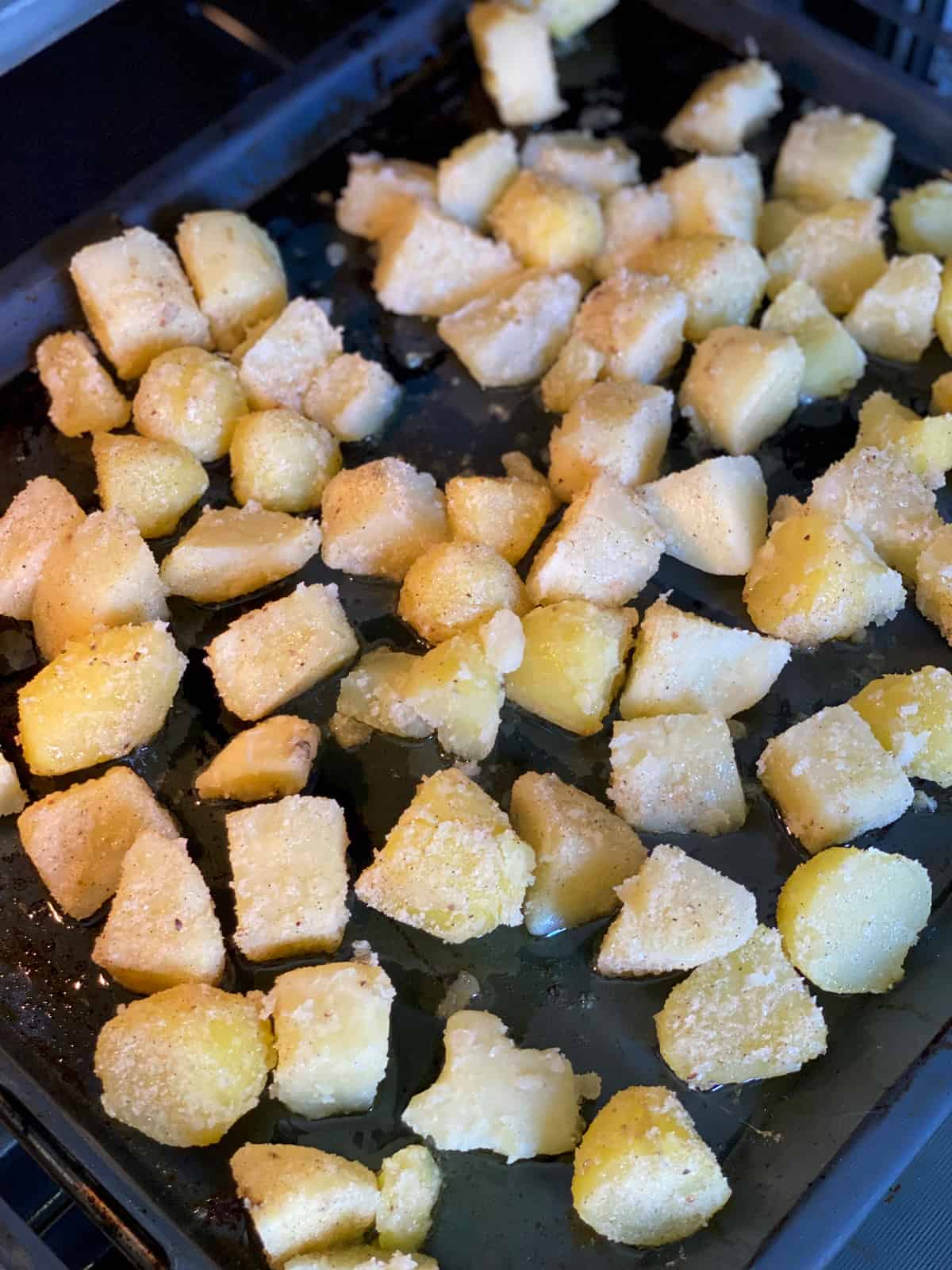 Potato pieces coated in a parmesan semolina in a roasting pan in the oven.