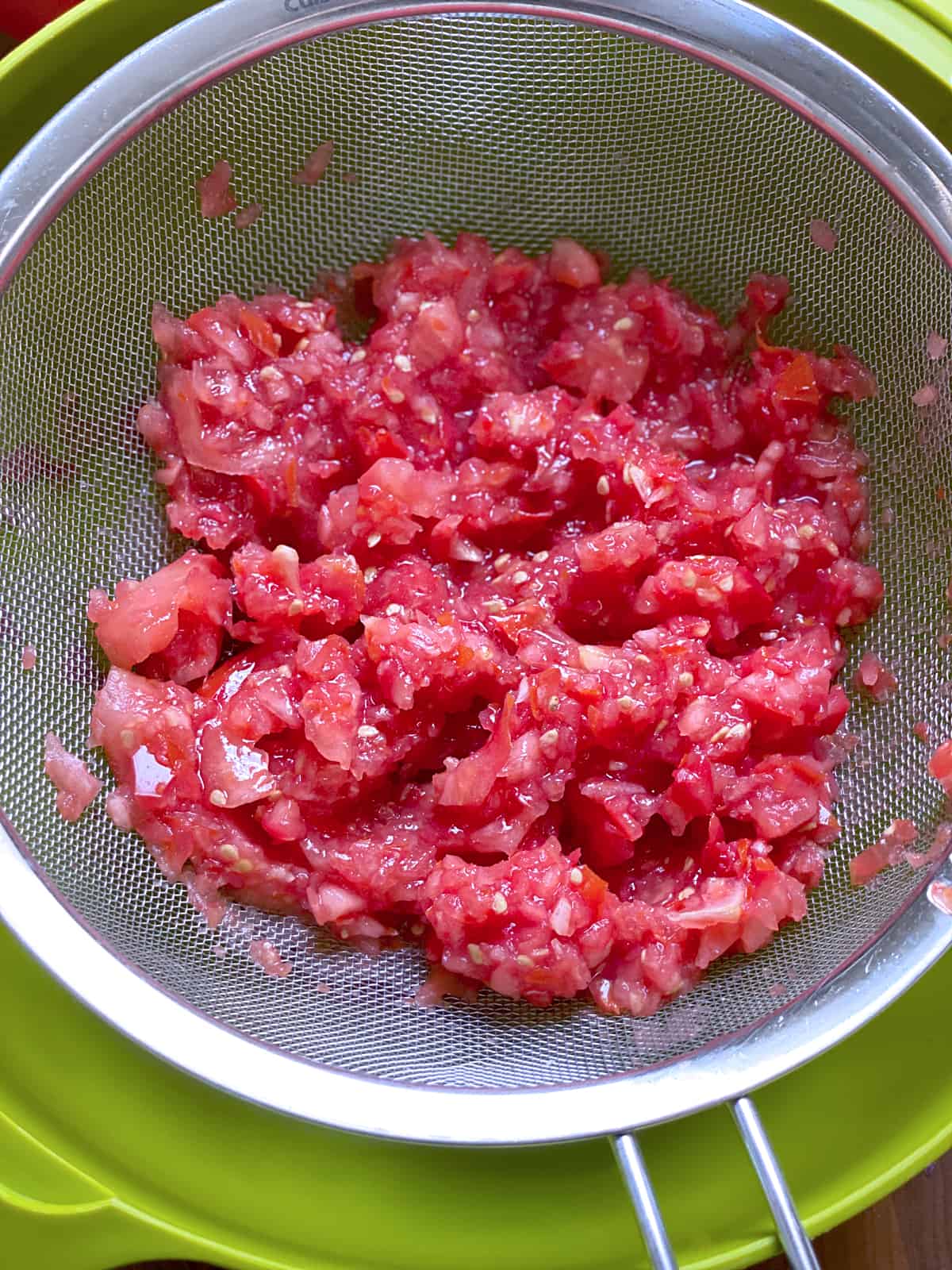 Grated tomatoes in a strainer over a bowl.