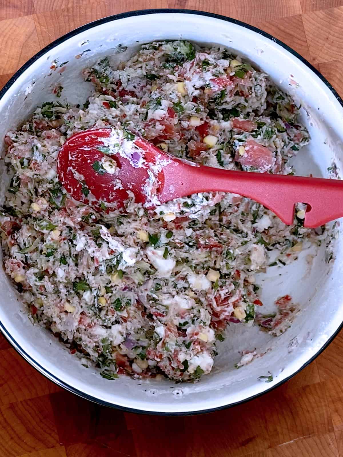 A white bowl with mix for tomato fritters and a red silicon spoon.
