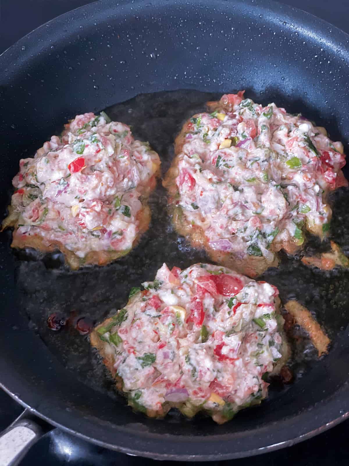 Three tomato fritters frying in a skillet.