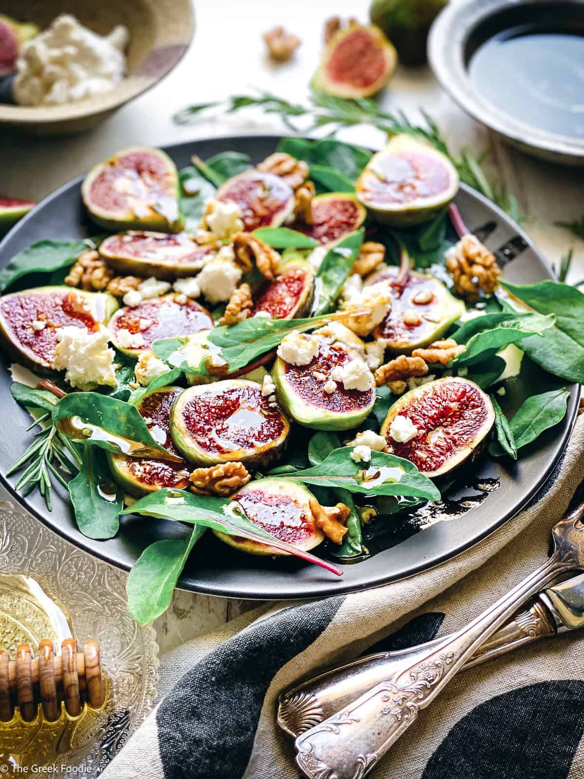 Overhead view of a Greek fig salad with beet greens, mizythra cheese and toasted walnuts on a dark plate.