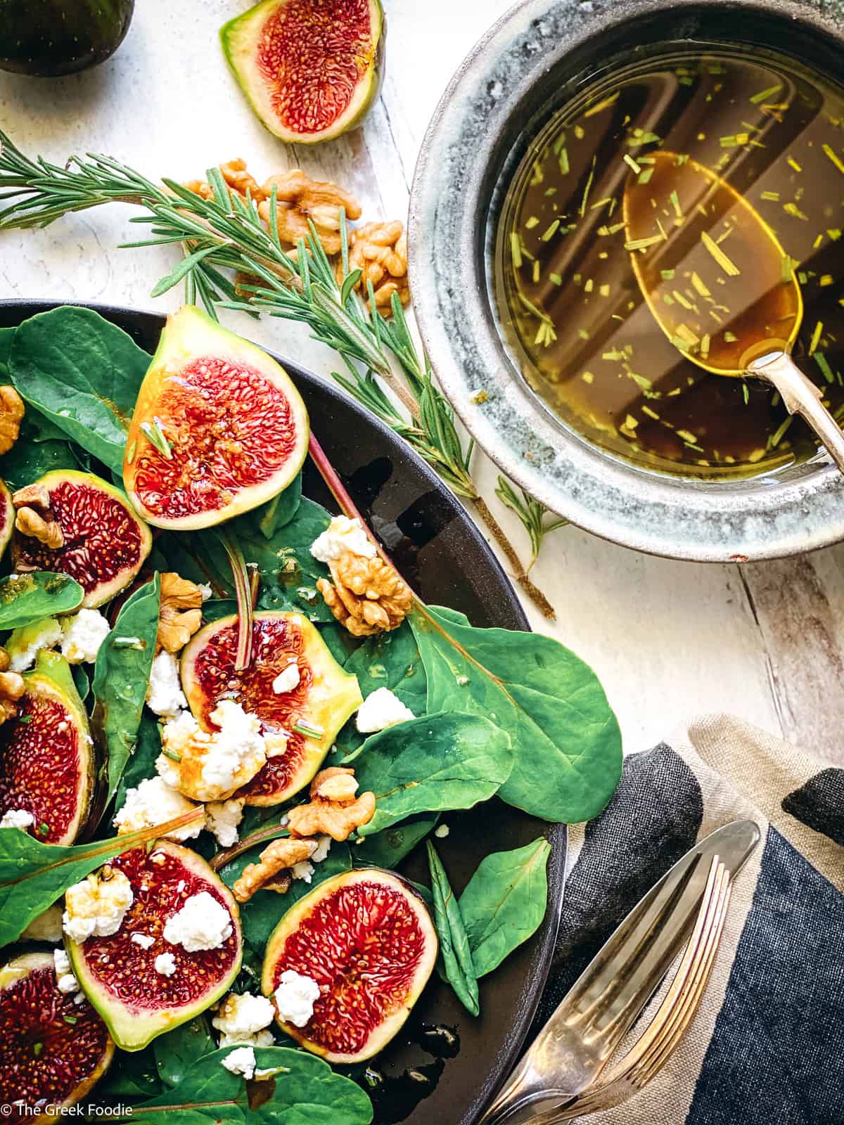 Rosemary balsamic vinaigrette being spooned from a bowl beside a plate of fig salad with walnuts and mizythra.