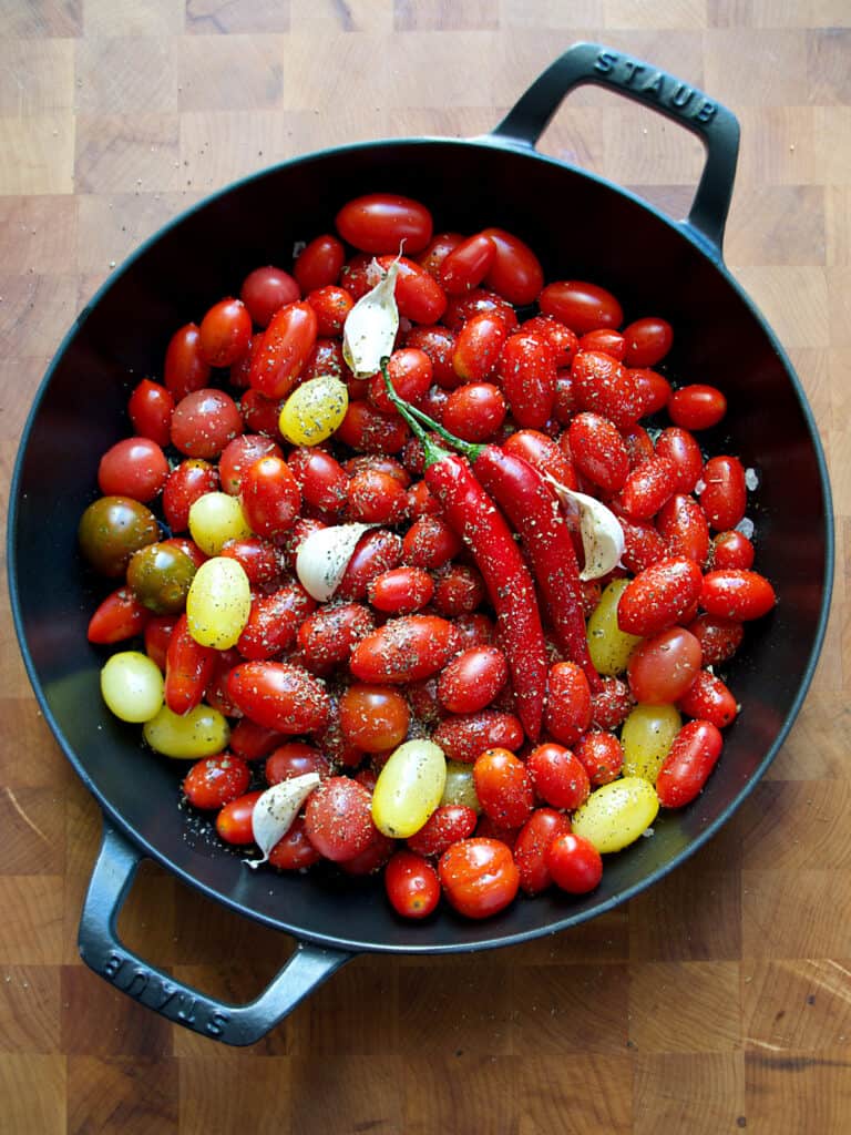 Cherry tomatoes, garlic cloves and chili peppers in a large cast iron pan.
