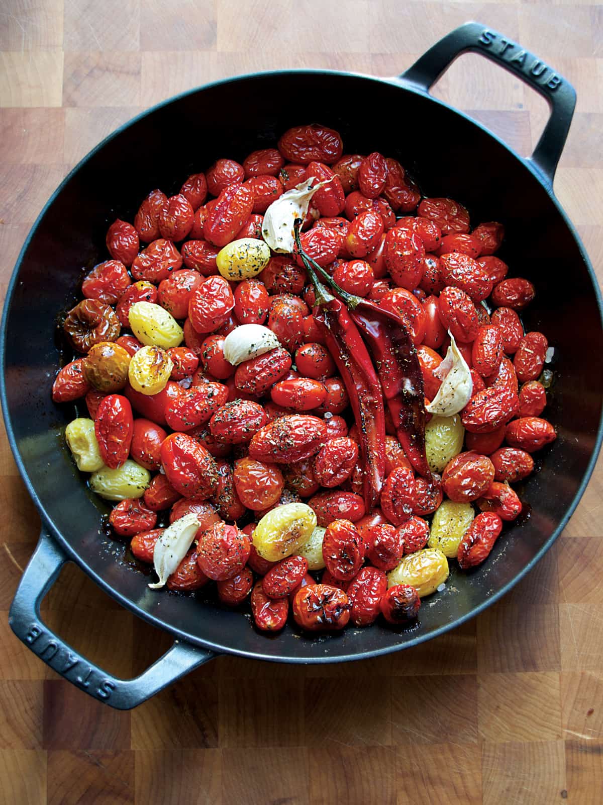 Roasted cherry tomatoes and chili peppers in a large cast iron pan.