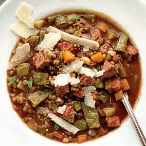 A bowl with lentil sausage soup and a spoon.