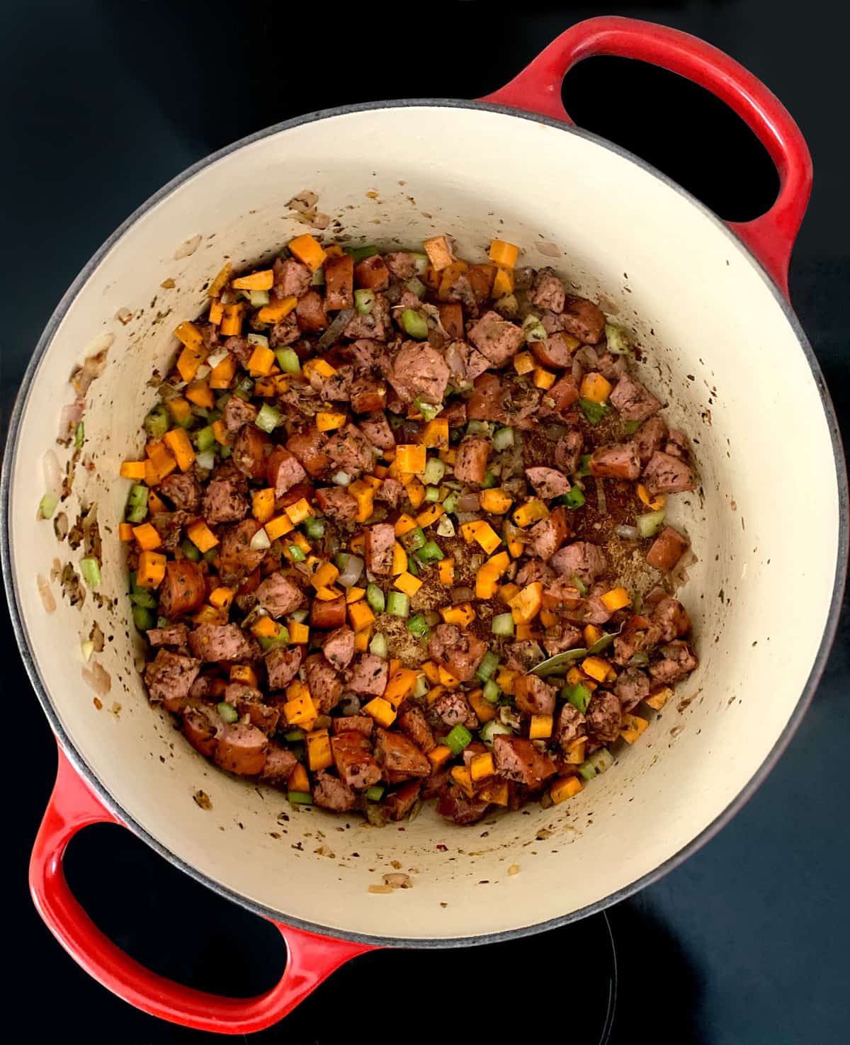 Cut up sausage and diced vegetables with olive oil in a stockpot.