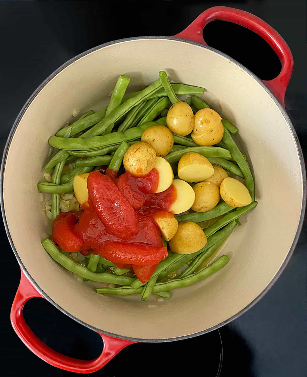 Green beans, potatoes and whole tomatoes in a stockpot.