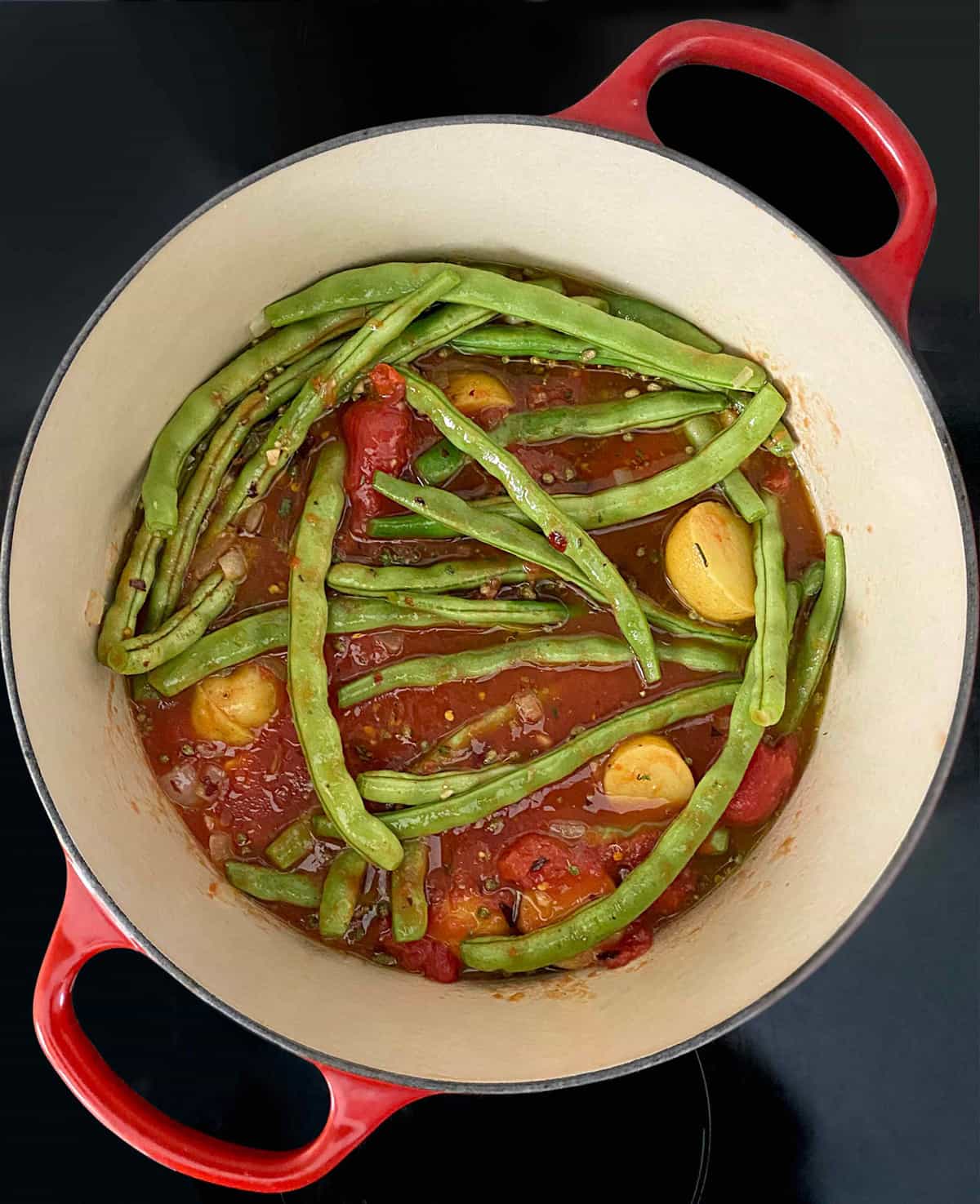 Green beans, potatoes and whole tomatoes in a stockpot.