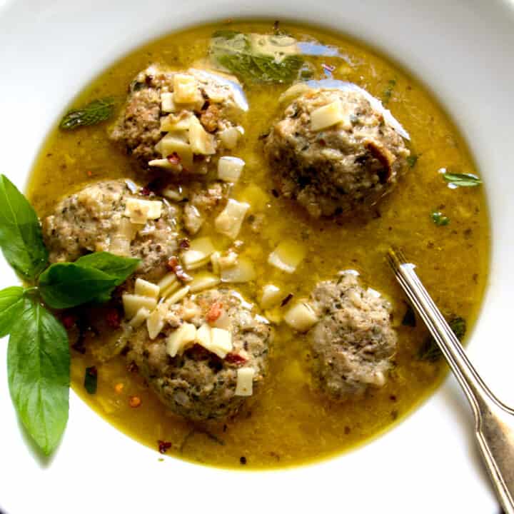 A bowl with meatball soup and a spoon.