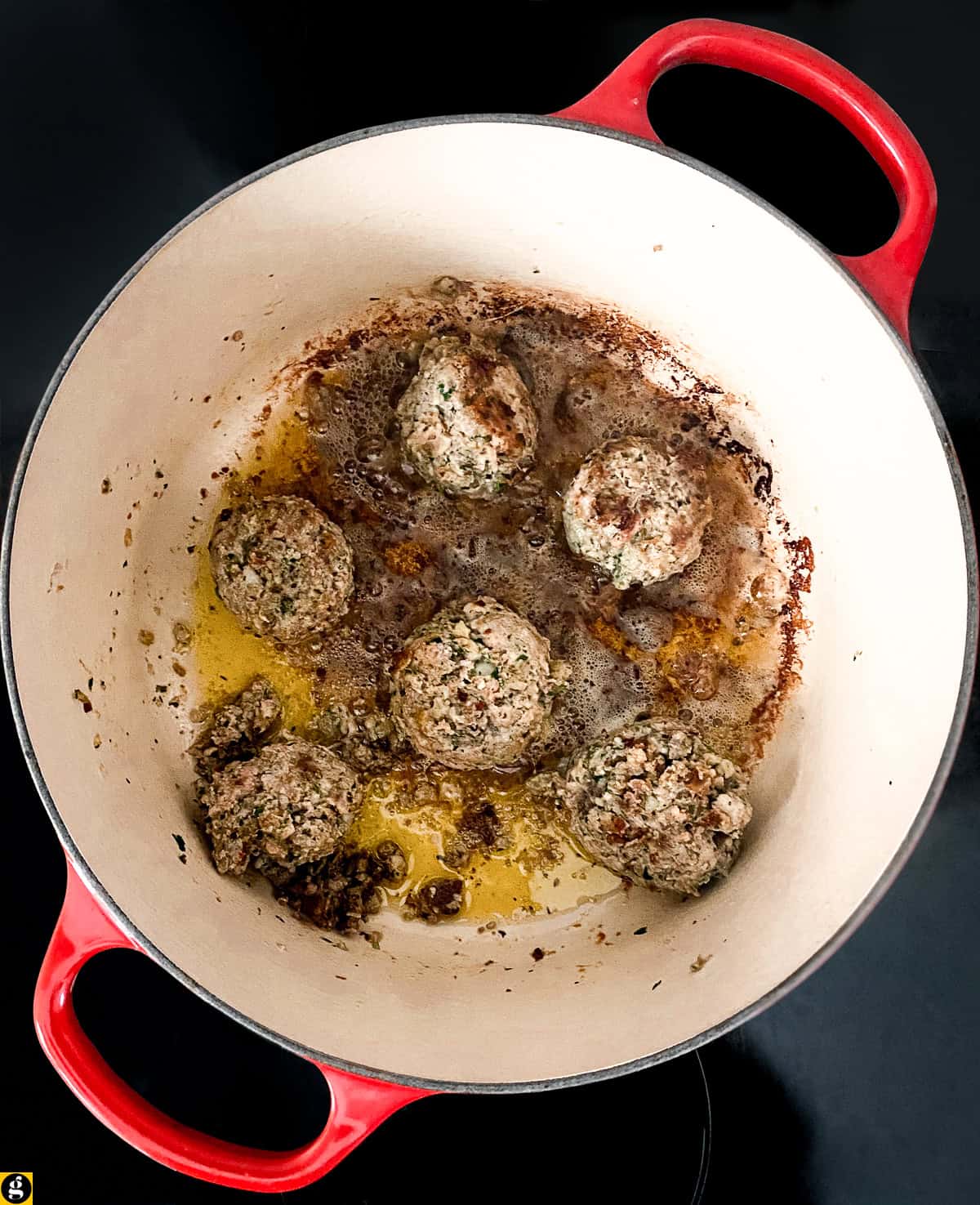 Meatballs browning in olive oil in a red Dutch oven.