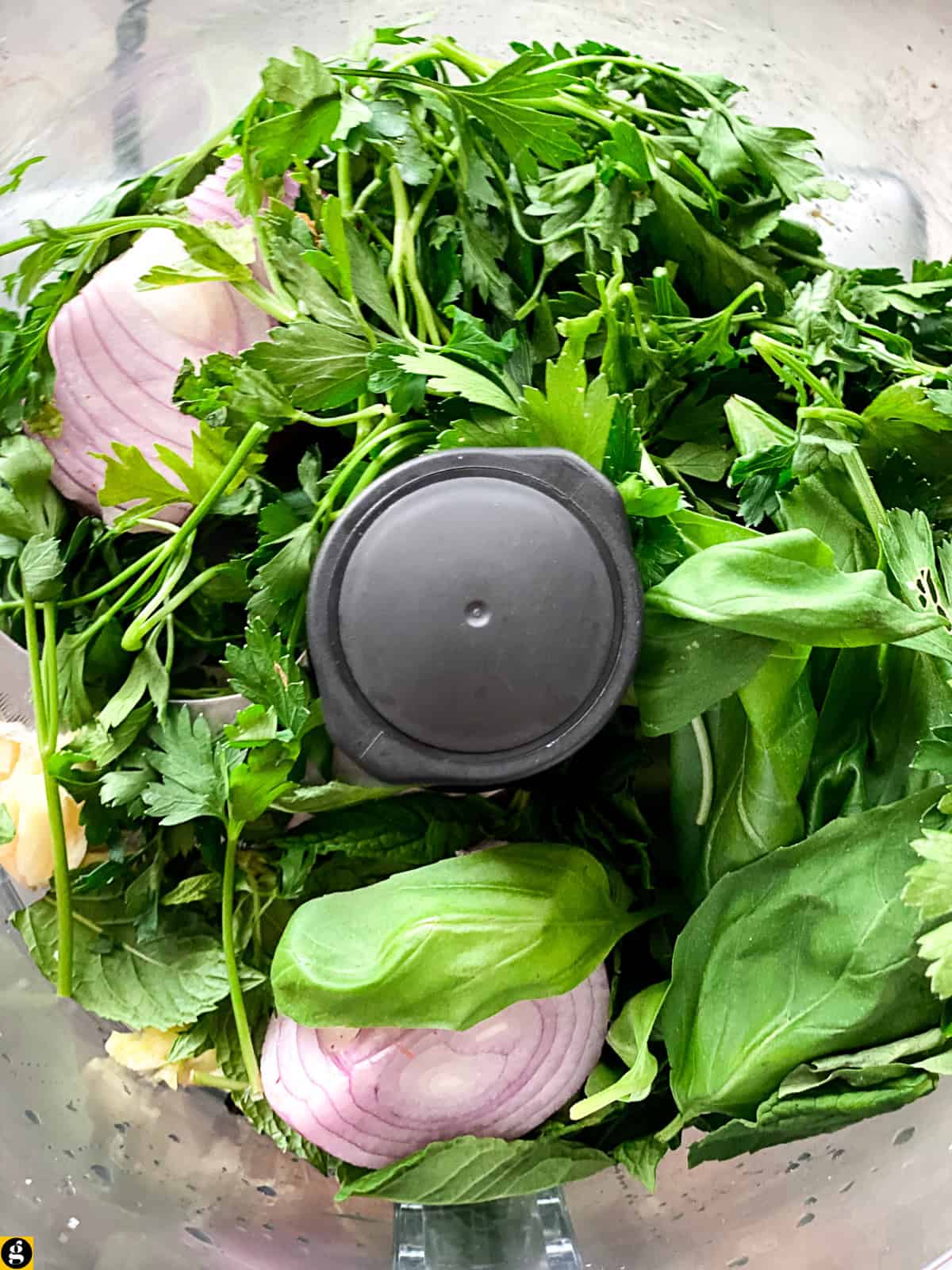 Fresh parsley, basil, spearmint, onion, and garlic in a food processor for meatball soup.